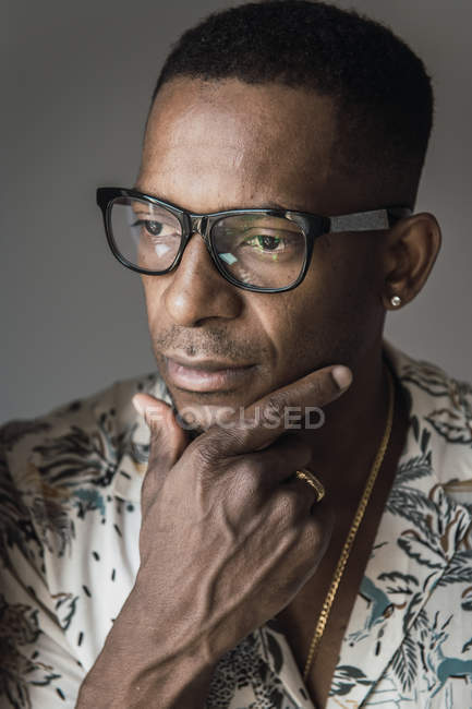 Portrait of serious African American man in golden accessories and glasses touching chin — Stock Photo