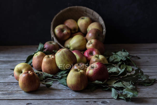 Pommes fraîches mûres et feuilles avec panier sur table rustique en bois — Photo de stock