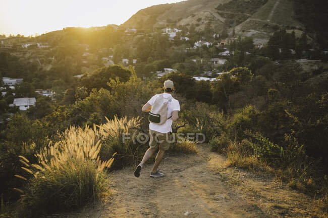 Back view of anonymous guy with backpack running along countryside path during wonderful sunset in Los Angeles, California — Stock Photo
