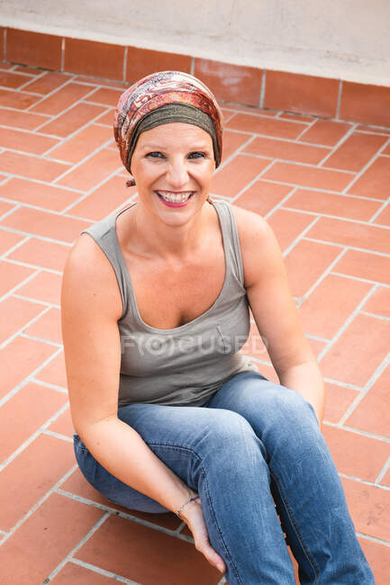 De cima vista de mulher sorridente em pano de cabeça sentado no chão da telha e olhando para a câmera — Fotografia de Stock