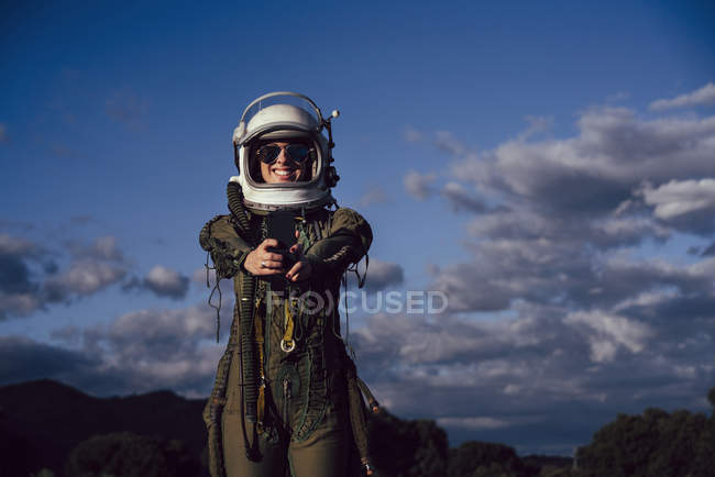 Female astronaut taking selfie with mobile phone against evening sky in nature — Stock Photo