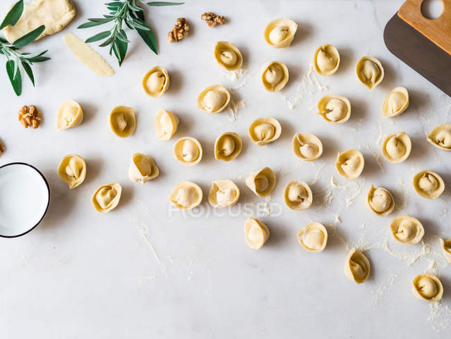 Handmade tortellini on white background with herb leaves and flour — Stock Photo