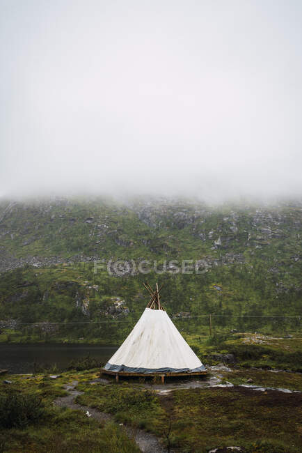 Barraca branca colocada em terreno verde na parte inferior da montanha coberta com densa névoa branca — Fotografia de Stock
