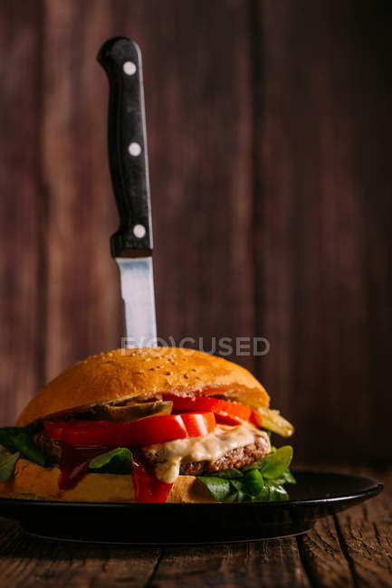 Delizioso hamburger gourmet con coltello su piatto su sfondo di legno scuro — Foto stock