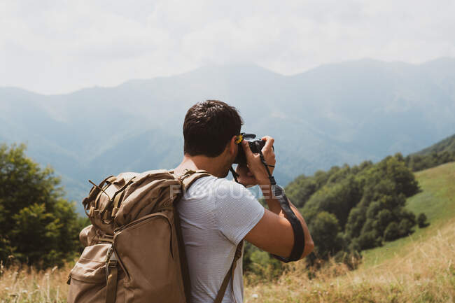 Vista posteriore dell'uomo con lo zaino utilizzando la fotocamera professionale per fare foto della pittoresca campagna in Bulgaria, Balcani — Foto stock