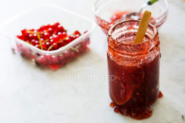 Glass jar of jam and plastic container with red currants on white background — Stock Photo