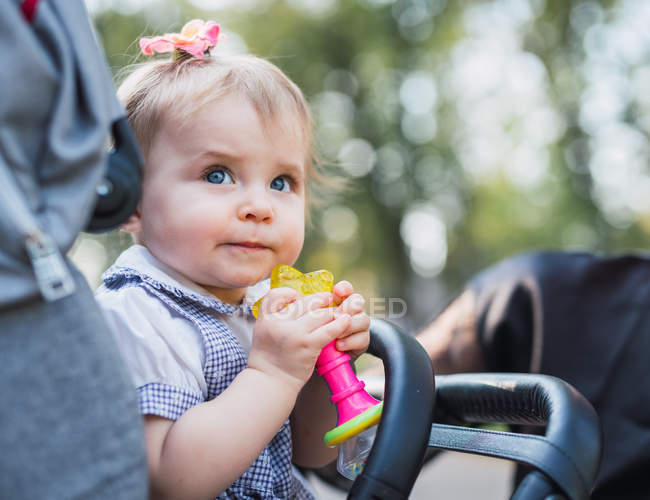 Cute baby girl holding toy in carriage outdoors — Stock Photo