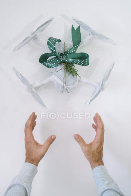 Mãos masculinas com drone embrulhado como presente de Natal com ramo de abeto e fita verde no fundo branco — Fotografia de Stock