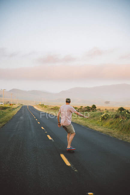 Side view of young man in casual outfit riding skateboard along asphalt countryside road in Point Reyes, California — Stock Photo