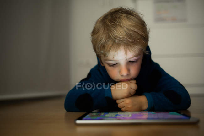 Маленький хлопчик дивиться мультфільми з цифровим планшетом на дерев'яній підлозі — стокове фото