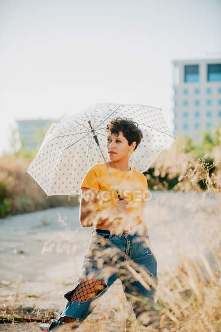 Вдумчивая молодая женщина с зонтиком, стоящая на улице и смотрящая в сторону — стоковое фото