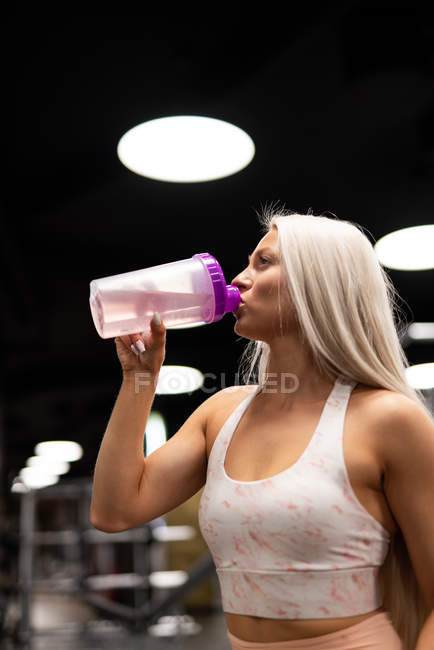 Молода блондинка спортсменка п'є воду в спортзалі — стокове фото