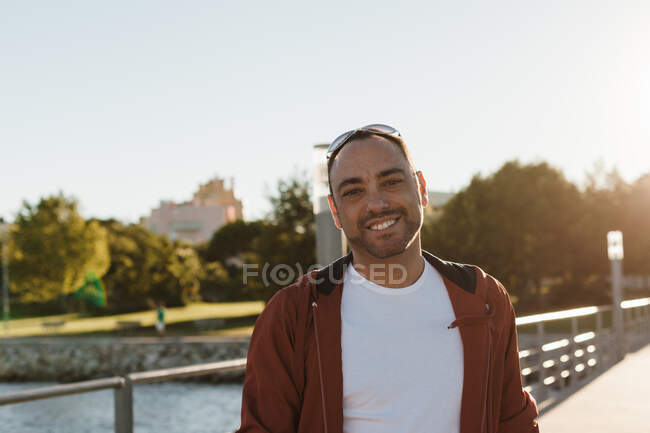 Handsome adult man in casual outfit looking at camera while standing on blurred background of beautiful autumn street on sunny day — Stock Photo