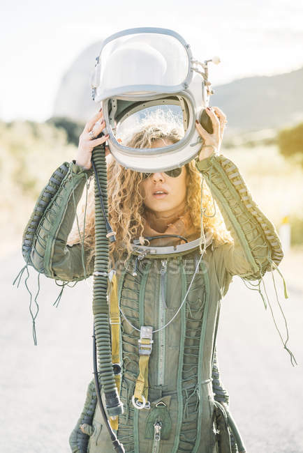 Confident woman in astronaut costume putting on helmet in sunlight — Stock Photo