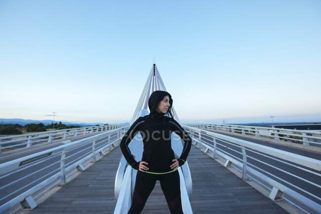 Mulher de sportswear preto em pé na construção moderna da ponte olhando confiante — Fotografia de Stock