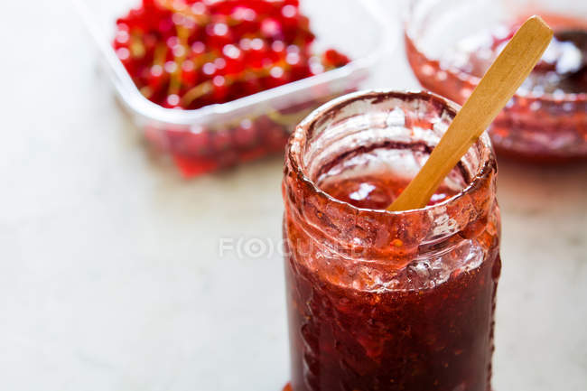 Glass jar of jam and plastic container with red currants on white background — Stock Photo
