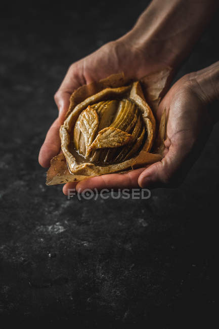 Mãos humanas segurando cozido maçã mini galette no fundo preto — Fotografia de Stock