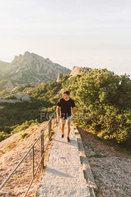 Attractive young guy in casual outfit walking along concrete mountain path and admiring view in beautiful morning in Barcelona, Spain — Stock Photo