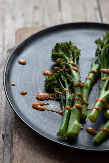 Primer plano de brócoli al vapor con salsa romesco en plato negro sobre mesa de madera - foto de stock