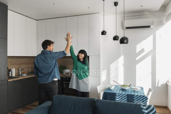 Cheerful young man and woman giving high five to each other while standing in modern kitchen together — Stock Photo
