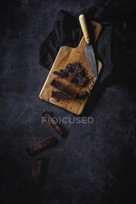 Schokoladenstücke und Brocken auf Holzbrett auf schwarzem Hintergrund — Stockfoto