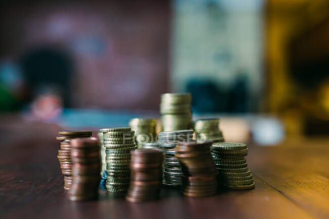 Tiro de close-up de pilhas de pequenas moedas deitadas na mesa de madeira no fundo borrado — Fotografia de Stock
