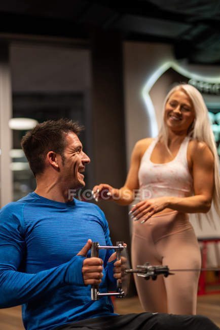 Hombre haciendo ejercicio en el gimnasio con la mujer de pie y sonriendo - foto de stock