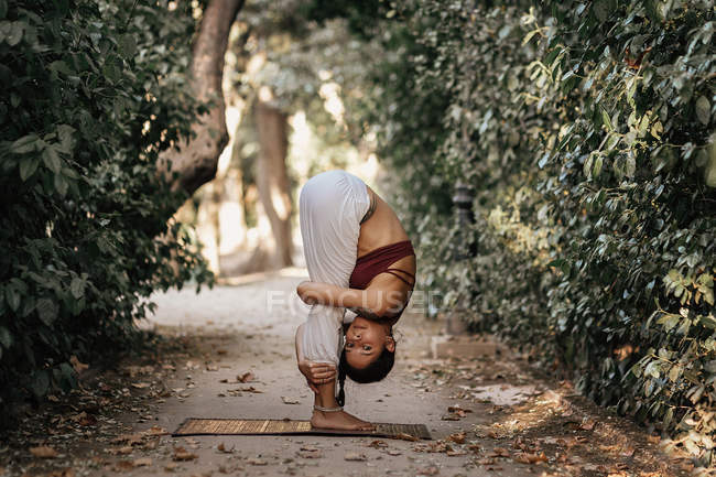Slim woman bending while doing yoga on alley in autumn park — Stock Photo