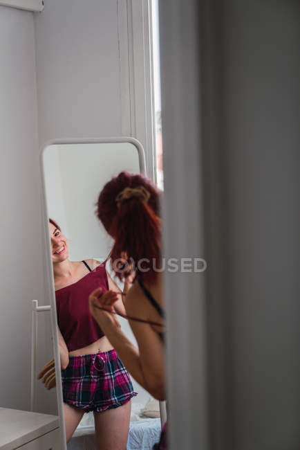 Lächelnde junge Frau, die vor dem Spiegel steht und Spaß hat — Stockfoto