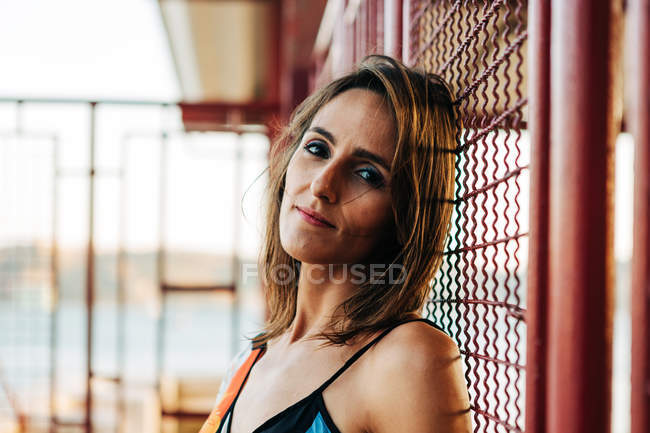 Portrait of content woman leaning on metal wire fence outdoors — Stock Photo