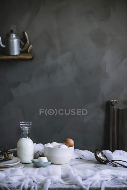 Schüssel mit Hühnereiern und Flasche frischer Milchprodukte steht auf Marmortischplatte in der Küche — Stockfoto