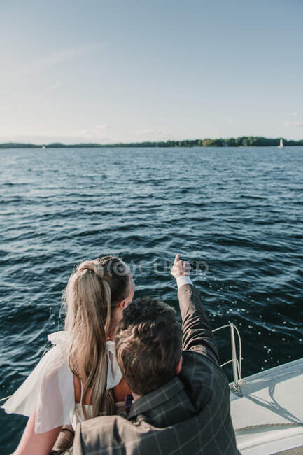 Back view of groom pointing away while standing with bride on boat on lake — Stock Photo