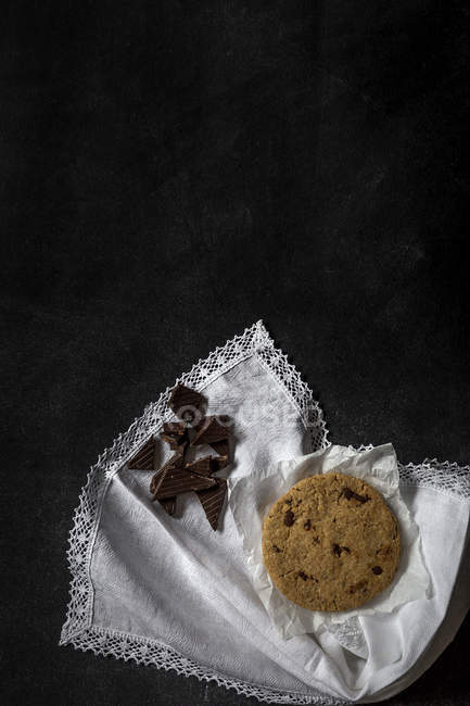 Galleta de chocolate con trozos de chocolate sobre servilleta blanca sobre fondo negro - foto de stock