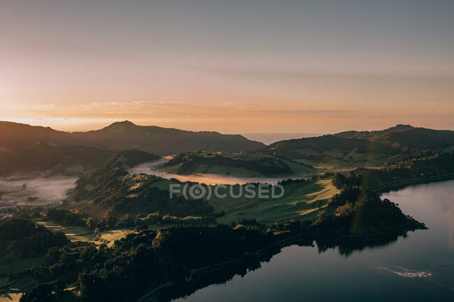 Sauberer stiller See mit Reflexion der Bäume vor dem Hintergrund von Kratern und Bergen unter wolkenlosem Himmel — Stockfoto