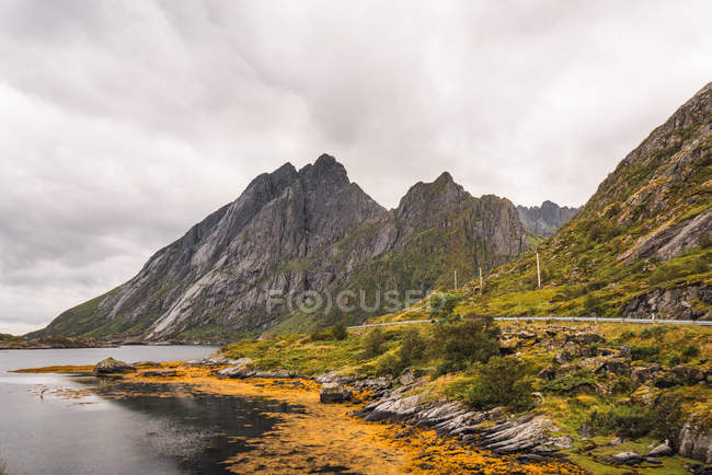 Paisagem de montanhas rochosas perto do lago com água colorida em amarelo sob céu nublado — Fotografia de Stock