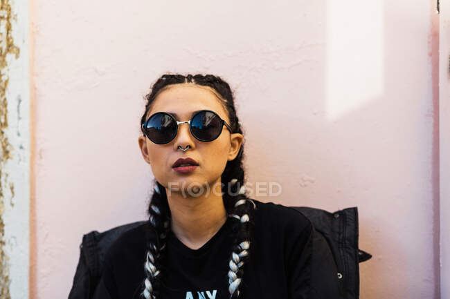 Модная брюнетка с пирсингом в солнцезащитных очках уверенно смотрит в камеру — стоковое фото