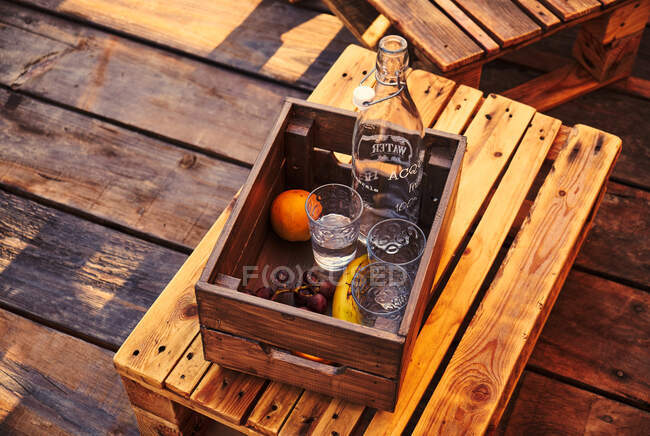 From above view of three glasses with bottle and grapes with banana and orange lying in wooden crate on chair — Stock Photo