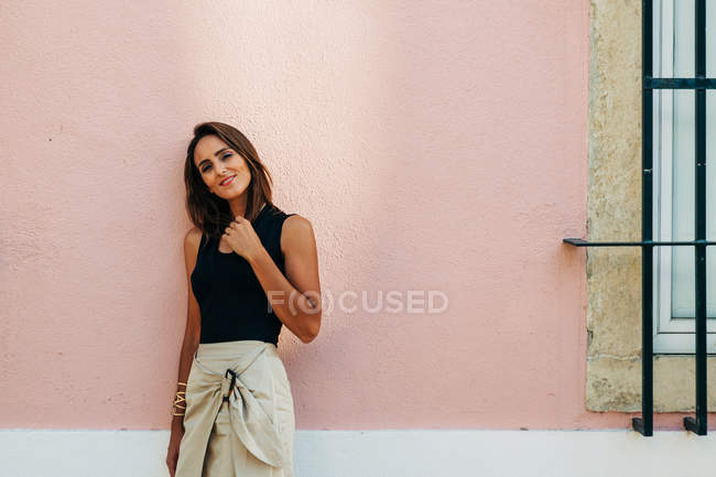 Charming brunette woman in trendy outfit leaning on wall on street and looking at camera — Stock Photo