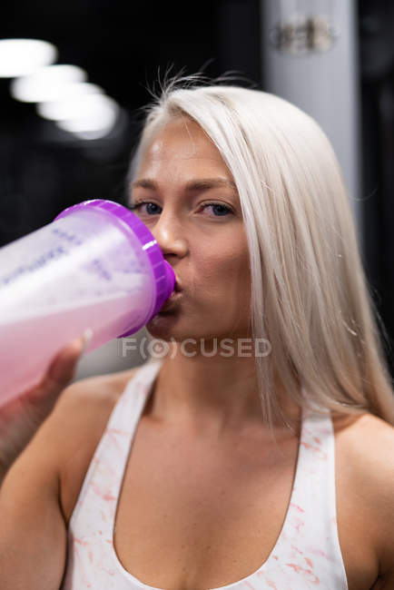 Close-up of young blond sportswoman drinking water in gym — Stock Photo
