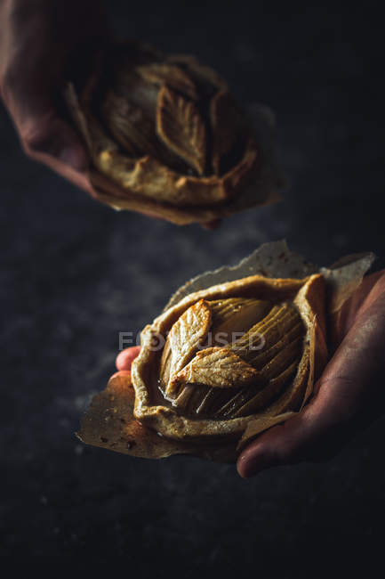Human hands holding baked apple mini galettes on black background — Stock Photo