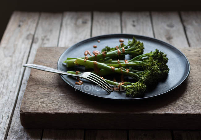 Brócolis cozido no vapor com molho romesco na placa preta com garfo na mesa de madeira — Fotografia de Stock