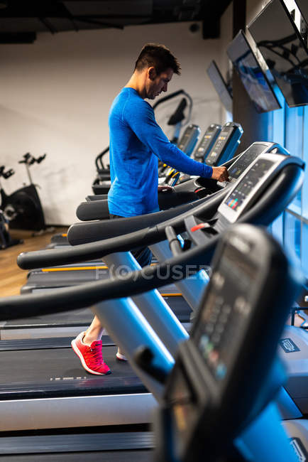 Joven en jersey deportivo azul haciendo ejercicio en la cinta de correr en el gimnasio - foto de stock