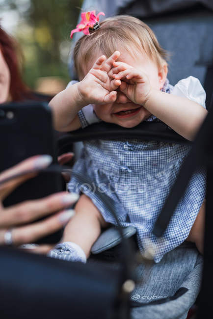 Female hand showing smartphone to crying baby girl while trying to cheer up in park — Stock Photo