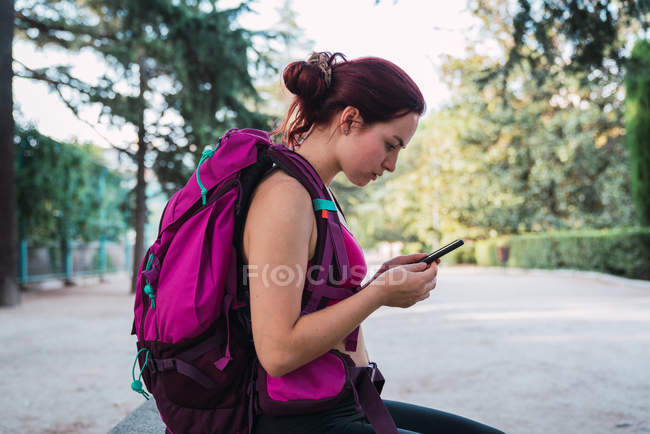 Спортсменка з рожевим рюкзаком, що переглядає смартфон у парку — стокове фото