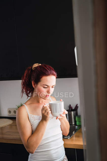 Young woman drinking coffee in kitchen — Stock Photo