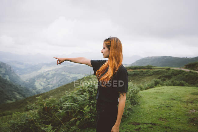 Seitenansicht einer attraktiven Frau in lässigem Outfit, die auf einem Berggipfel steht und an einem bewölkten Tag im herrlichen Kantabrien in die Ferne zeigt — Stockfoto