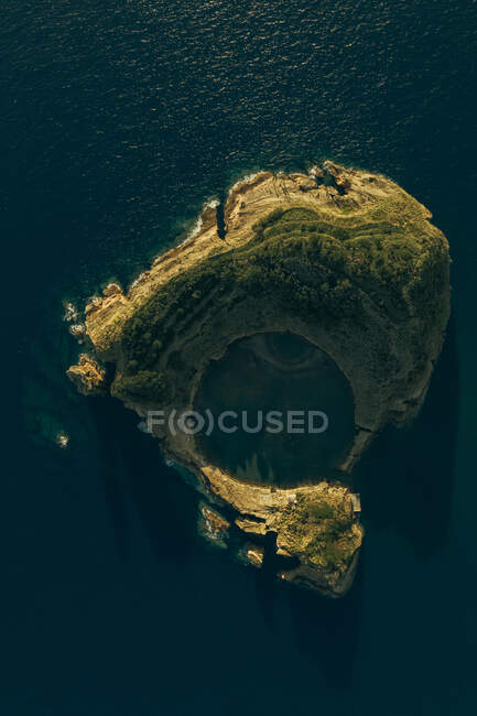 Вид с воздуха на маленький скалистый остров, омываемый спокойным голубым морем при дневном свете — стоковое фото