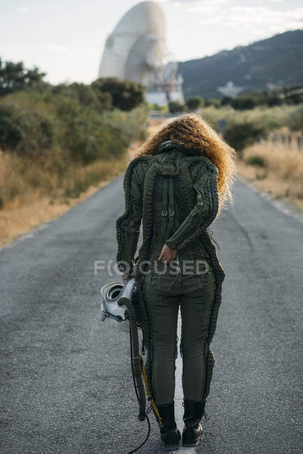 Back view of woman wearing astronaut costume walking along countryside road — Stock Photo