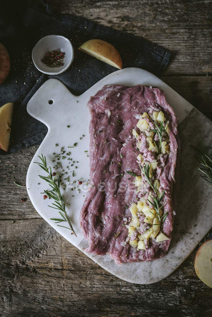 Mela tagliata e rosmarino fresco su fetta di carne cruda su tavolo di legno — Foto stock