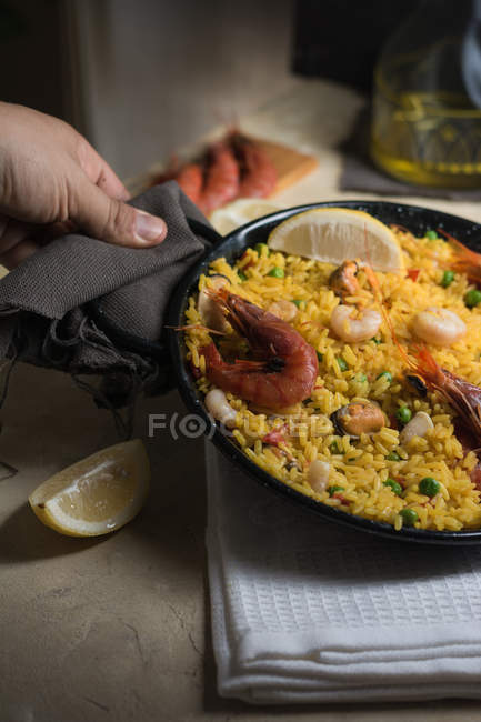 Human hand holding pan of traditional spanish paella marinera with rice, prawns, squid and mussels — Stock Photo